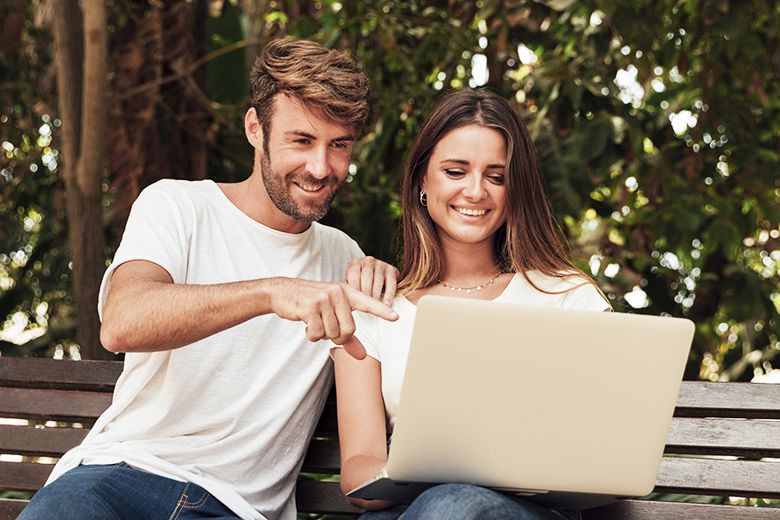 Férfi és nő túraútvonalat tervez laptopon, padon ülve egy parkban.